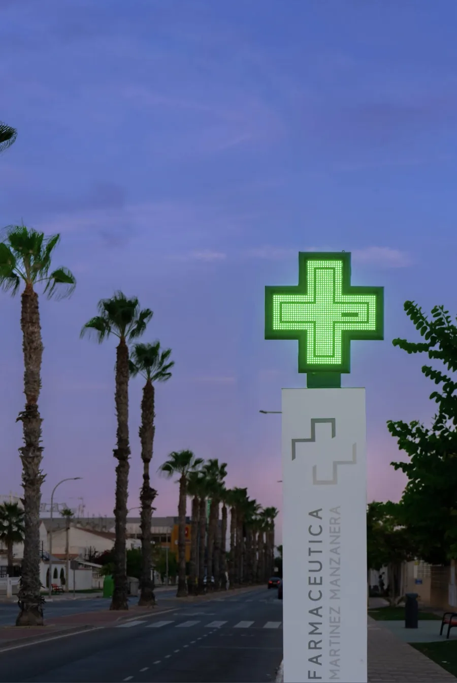 Cruz verde de Farmacia MM iluminada al atardecer, junto al Mar Menor